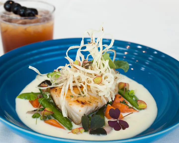 Salmon dinner on a blue plate with a cocktail next to it